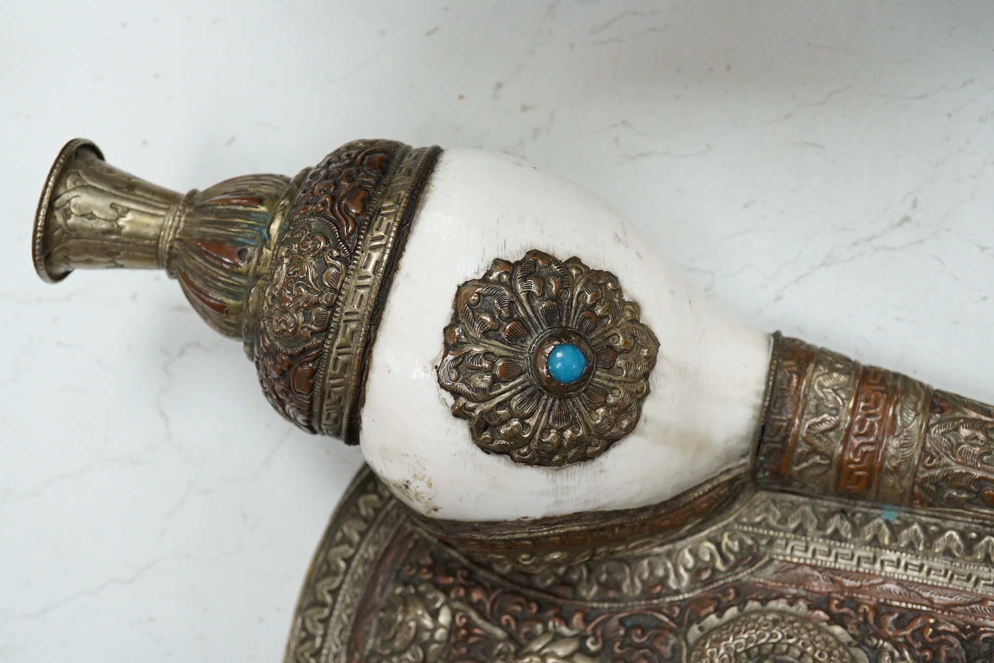 A Tibetan repoussé work cowrie shell trumpet, early 20th century, set with a cabochon, 37cm high. Condition - fair to good